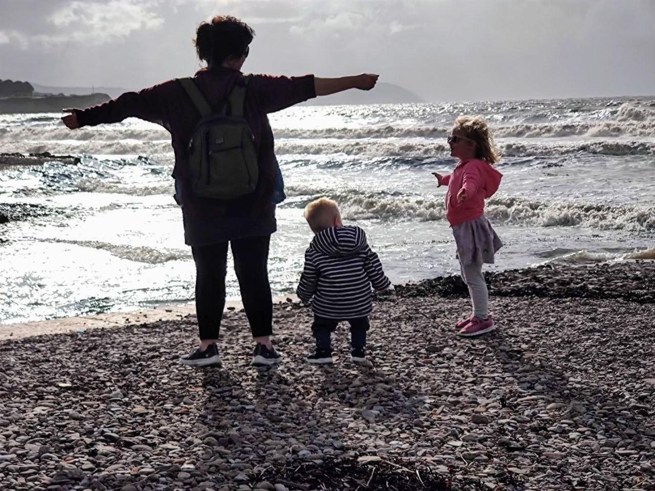 Lea and Her Children by the Sea | Lea's Getaways Lea, founder of Lea's Getaways, with her two children on rocks beside the sea during a family holiday.